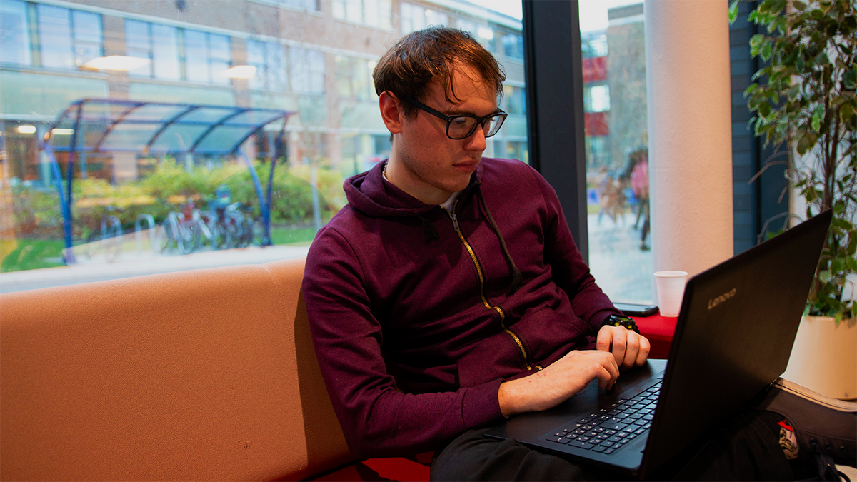 Student sitting in Minghella Studios foyer on sofa using laptop.