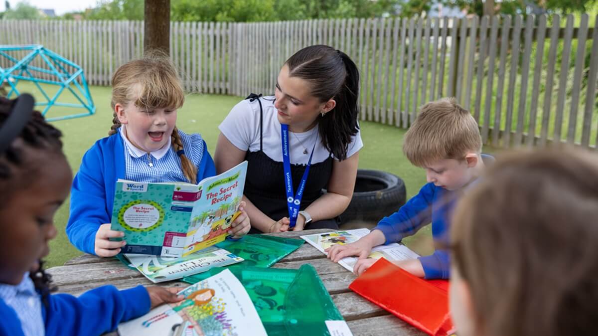 A teacher reading with pupils outside