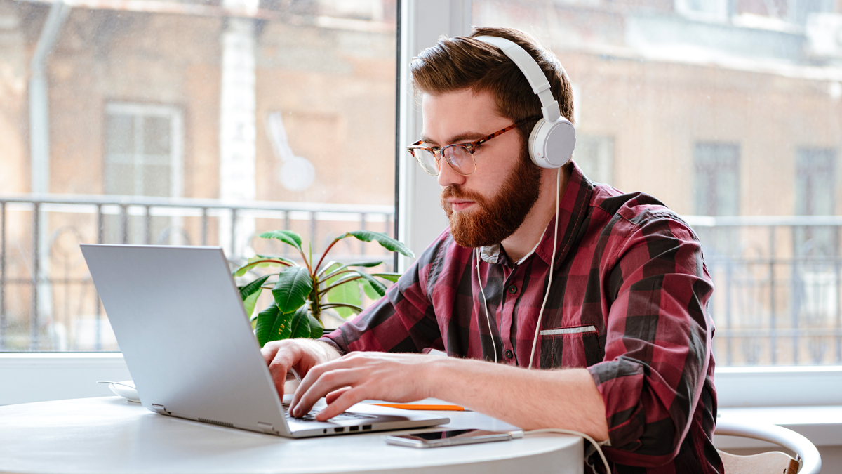 Male student working on his laptop at a desk, wearing white headphones