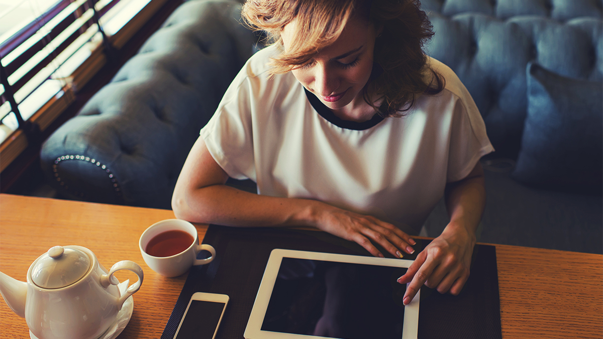 Student using tablet while drinking tea in a cafe